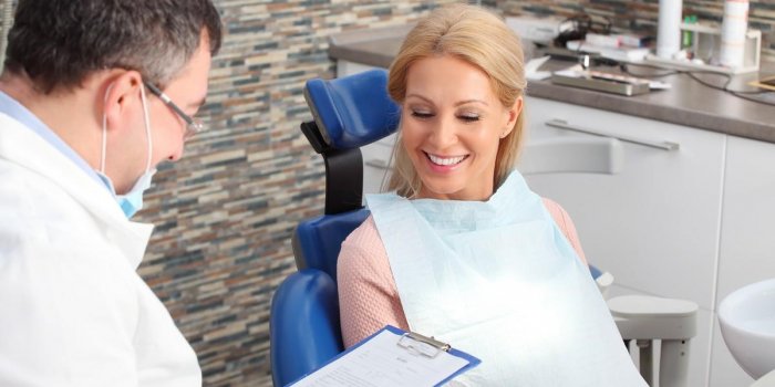 portrait of friendly male dentist holding in his hand a clipboard and consulting with his beautiful patient at dentist office