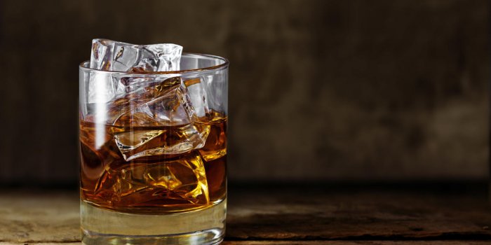 glass of scotch whiskey with ice cubes on a rustic wooden table, copy space in the brown background
