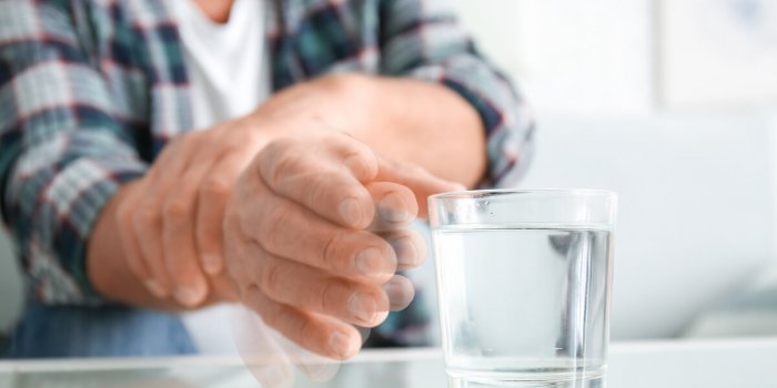 senior man with parkinson syndrome taking glass of water from table, closeup