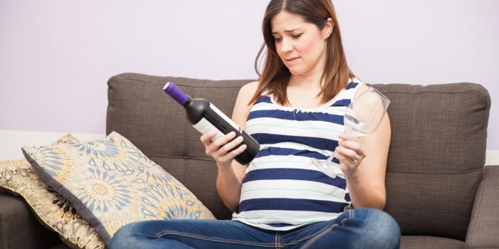pretty young pregnant woman holding a bottle of wine and glass and deciding whether to drink wine or not