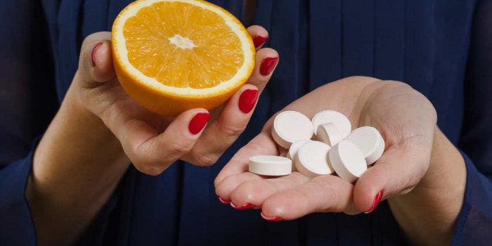 a woman holds a natural vitamin-orange in one hand and a synthetic vitamin c in the other makes a choice