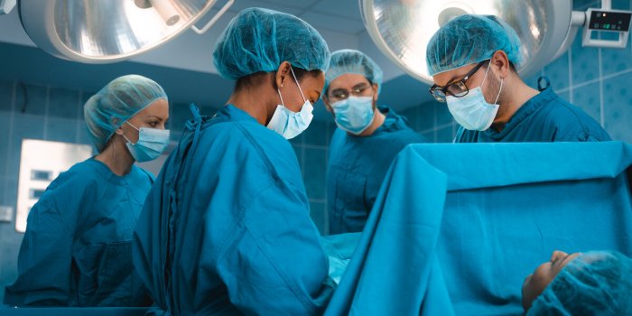 professional medical team of concerted serious surgeons wearing operating gowns performing chest operation on lying patie...