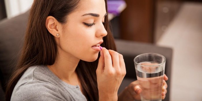 cute young brunette taking a pill with a glass of water at home