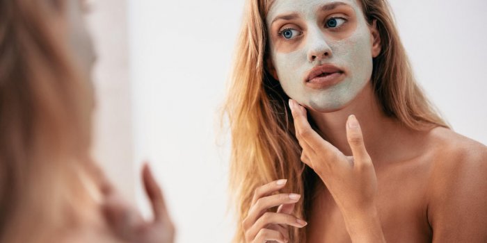 femme regardant dans le miroir avec masque sur son visage femme appliquant un masque cosmétique dans salle de bain
