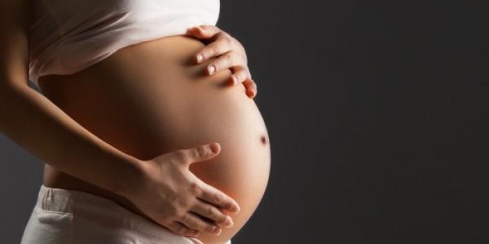 femme enceinte caresse son ventre sur fond gris