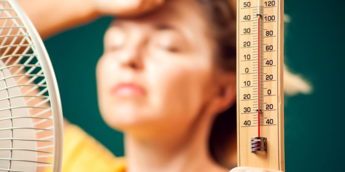 a portrait of woman in front of fan suffering from heat holding thermometer close up hot weather concept