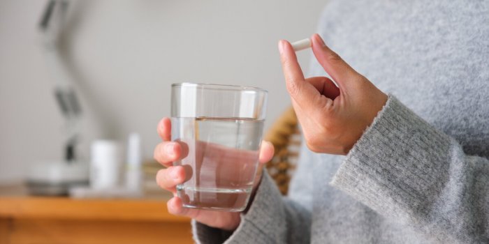 closeup image of a woman holding white pills and a glass of water