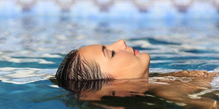 vue de côté d'un visage de femme relaxant flottant sur l'eau d'une piscine ou d'un spa