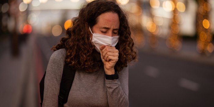 caucasian woman wearing a protective mask and coughing in the streets