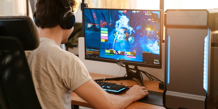 caucasian brunette guy in headphones playing video game on his computer while sitting at home