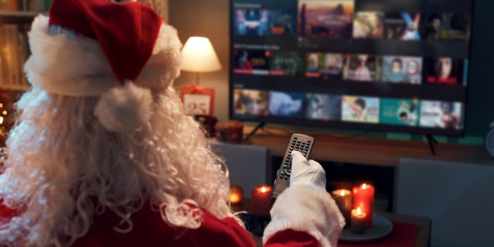 santa claus relaxing on the couch at home and watching tv, he is choosing a movie on the video on demand menu