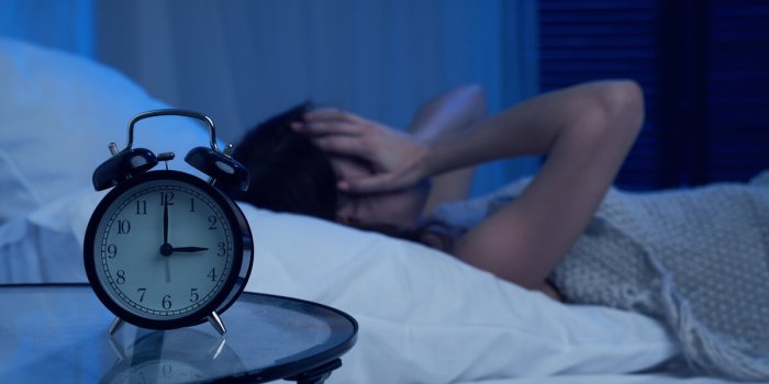 woman with insomnia lying on bed next to alarm clock at night in apartment