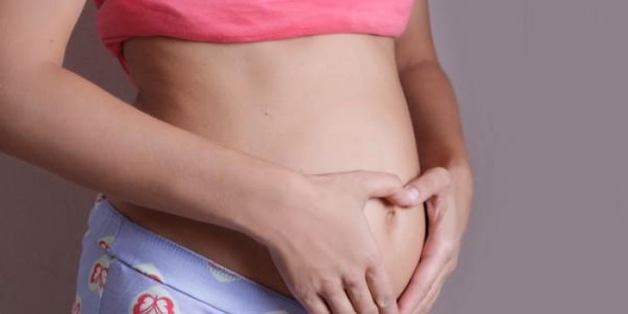 femme tenant par la main en forme de coeur sur son ventre de femme enceinte