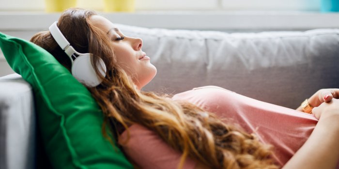 portrait of a beautiful young woman lying on sofa with headphones on and closed eyes, relaxing