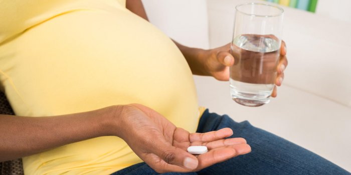 close-up of pregnant woman hand with glass of water and vitamin pill