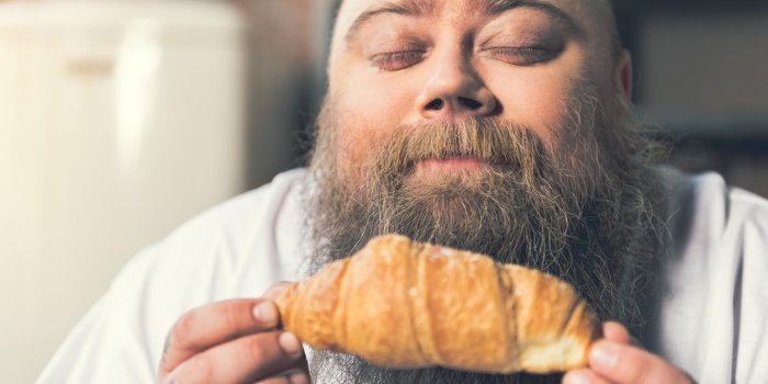 portrait of hungry thick man holding croissant and smelling it with enjoyment his eyes are closed