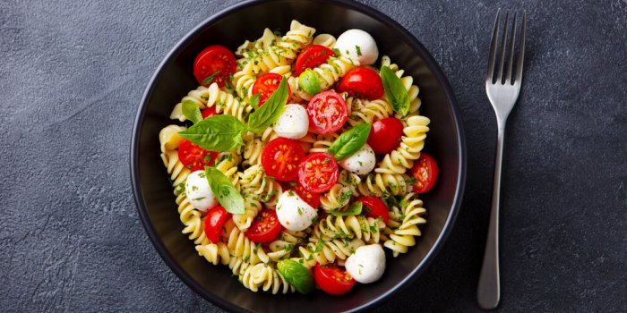 pasta fusilli with mozzarella cheese, tomatoes and basil dark background close up top view