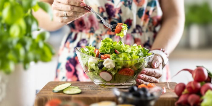 a portion of healthy salad on a fork in the hand of a young woman