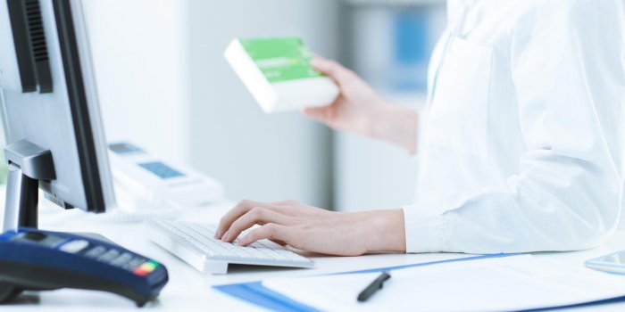 pharmacist holding a medicine packet and searching that product in the computer database, healthcare and technology concept