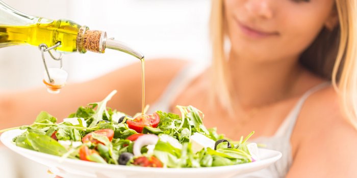 young happy blonde girl eating healthy salad from arugula spinach tomatoes olives onion and pouring olive oil