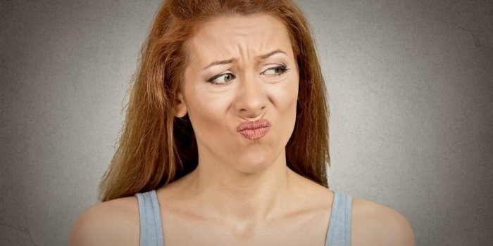 upset disgusted woman with displeased face expression isolated on grey wall background human emotion feeling body languag...
