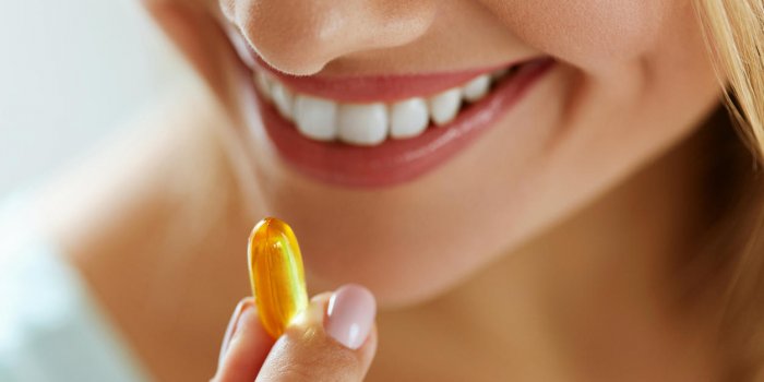 vitamin and supplement closeup of beautiful young woman taking yellow fish oil pill female hand putting omega-3 capsule i...