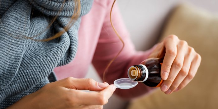 cropped view of ill woman with grey scarf taking cough syrup