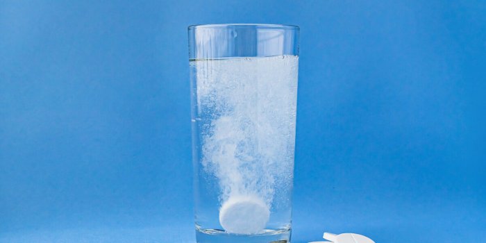 fizzy aspirin in a glass of water on a blue background vertical format and soft focus