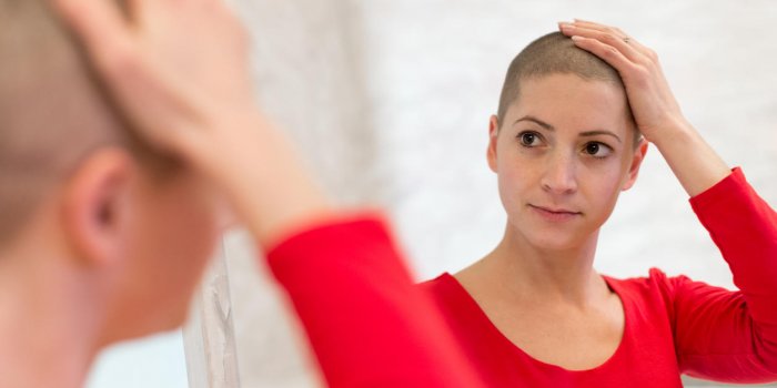 young adult female cancer patient looking in the mirror, stroking her new short hair