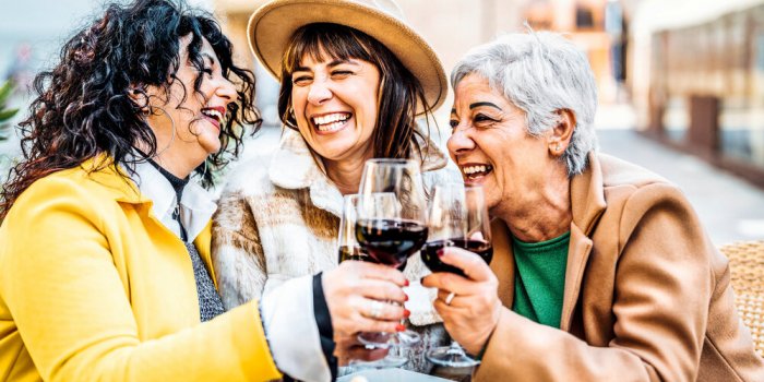 three happy retired female drinking and toasting red wine glasses at bar restaurant - group of happy elderly women having...