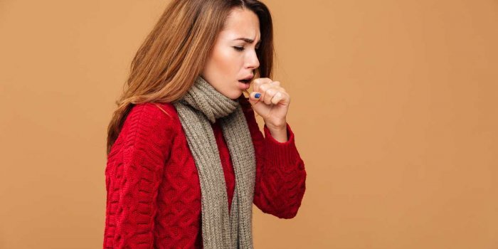 photo of young coughing brunette woman in warm wear, isolated over beige background