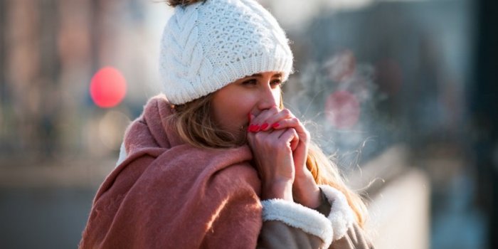 woman breathing on her hands to keep them warm at cold winter day