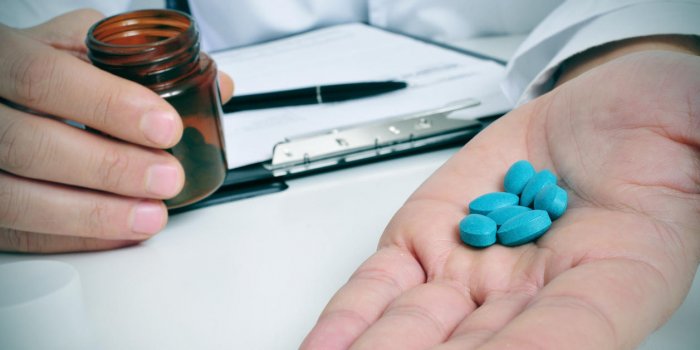 a doctor sitting in a desk with a pile of blue pills in his hand