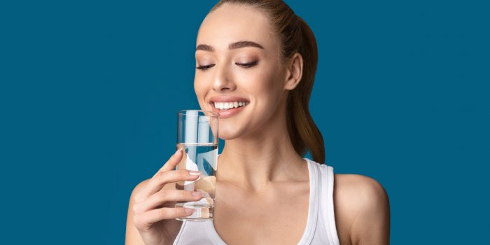 happy girl drinking glass of water standing on blue studio background healthy lifestyle concept