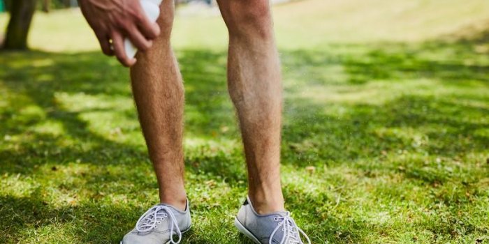 close-up of a man spraying insect repellent on his legs while outdoors