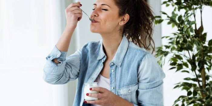 portrait of beautiful young woman eating yogurt at home