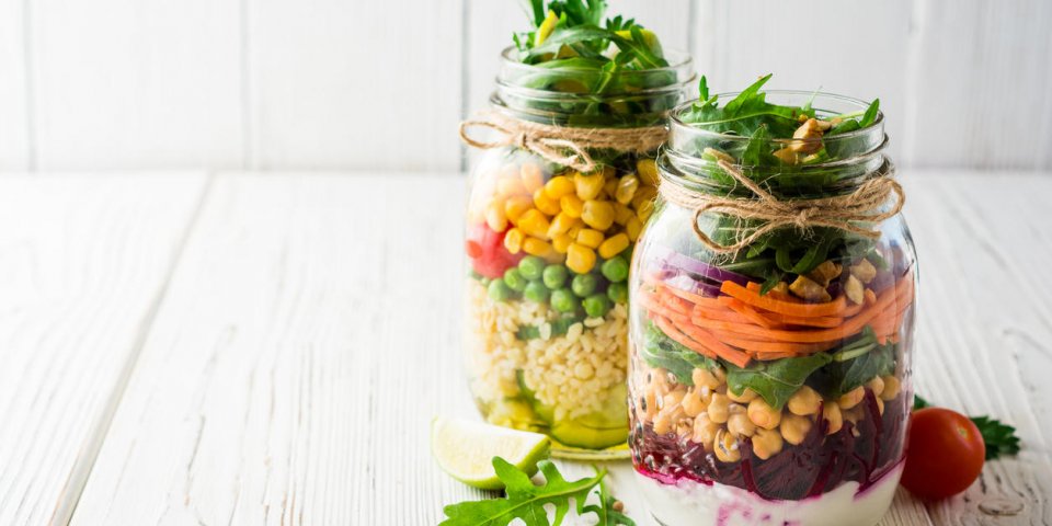 healthy homemade salads with chickpeas, bulgur and vegetables in mason jars on white wooden background selective focus co...