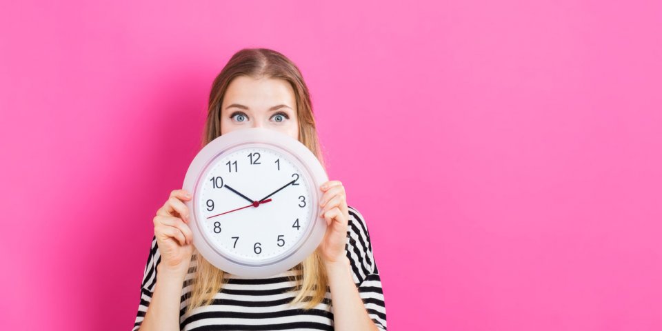 young woman holding a clock on a pink background