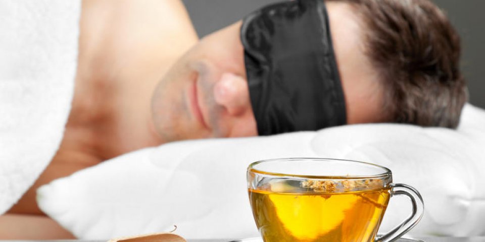 homme avec un masque de sommeil dormir sur un lit, une tasse de tisane au premier plan