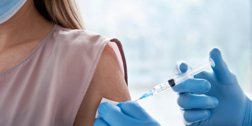 male doctor holding syringe making covid 19 vaccination injection dose in shoulder of female patient wearing mask flu inf...