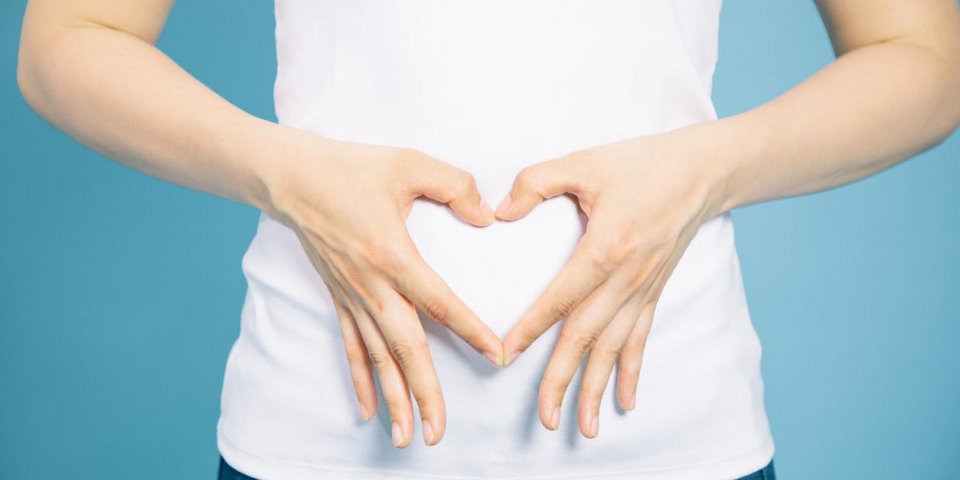 young woman who makes a heart shape by hands on her stomach