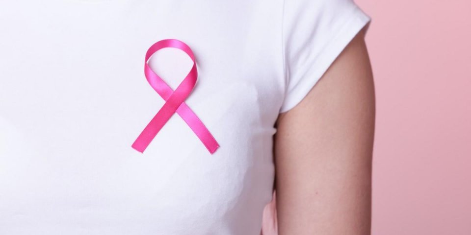 healthcare, medicine and breast cancer awareness concept - closeup of pink badge ribbon on woman chest to support breast ...