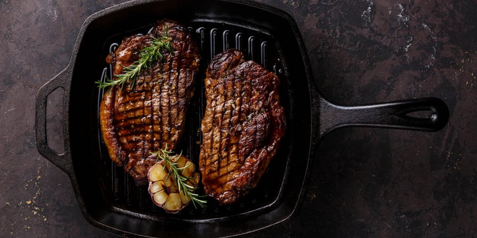 grilled black angus steak striploin on frying cast iron grill pan on dark background