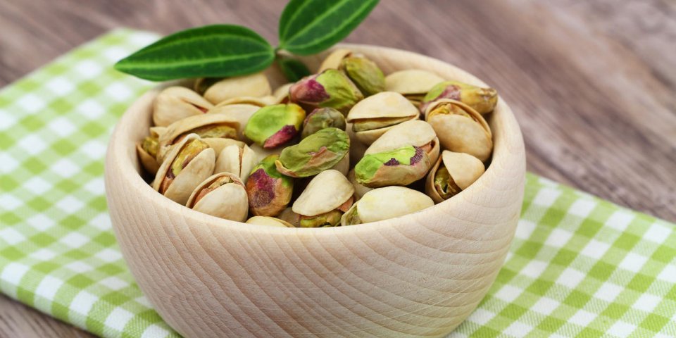 pistachio nuts in wooden bowl on checkered cloth