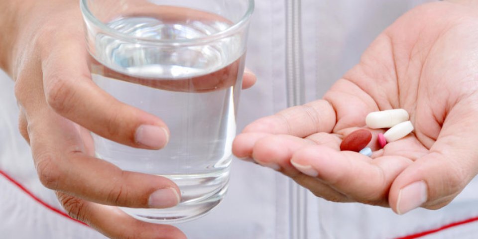 femme tenant une pilule et un verre d'eau à la main