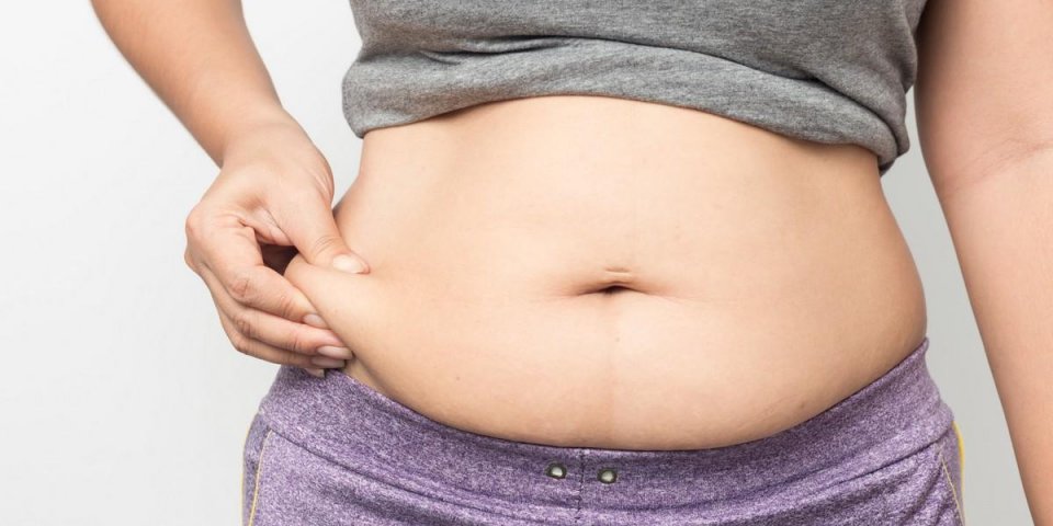 overweight woman hand pinching excessive belly fat on gray background, healthy concept