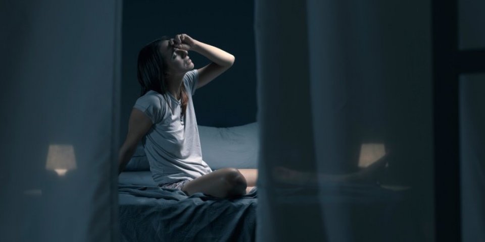 tired woman sitting in bed at night with open window, she is suffering from the heat and she is unable to sleep