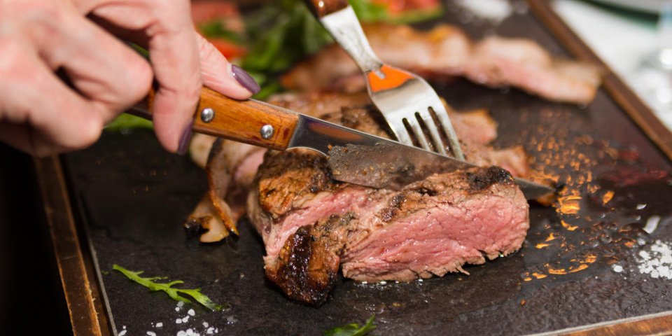 woman hand holding knife and fork cutting grilled beef steak on stoned plate selective focus