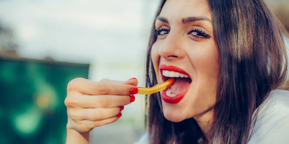 young woman eating french fries potato with ketchup in a restaurant, having her lunch break close up