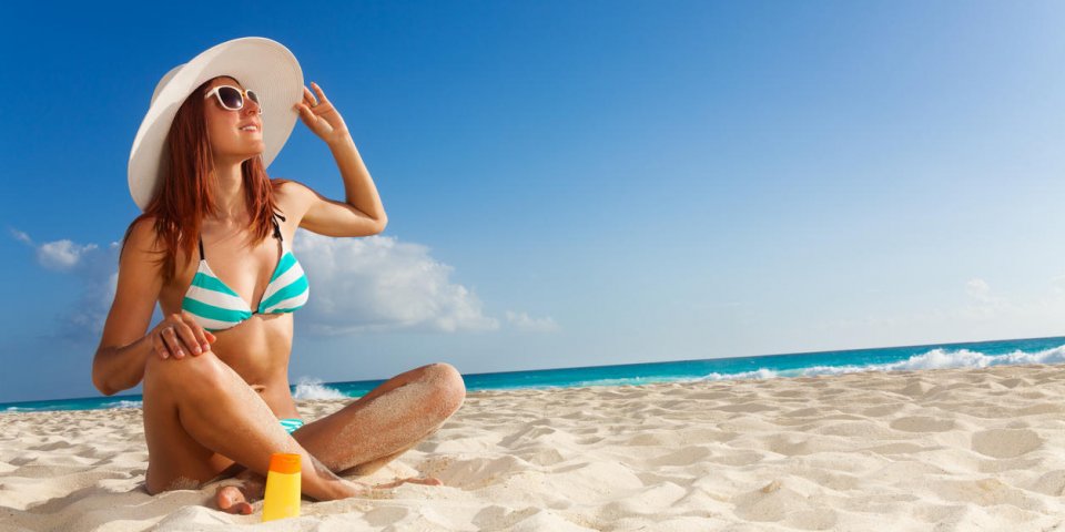 fille bronzée en bikini rayé bleu et grand chapeau blanc reposant sur la plage ensoleillée